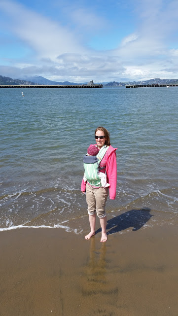Mother standing on beach with baby in a carrier.